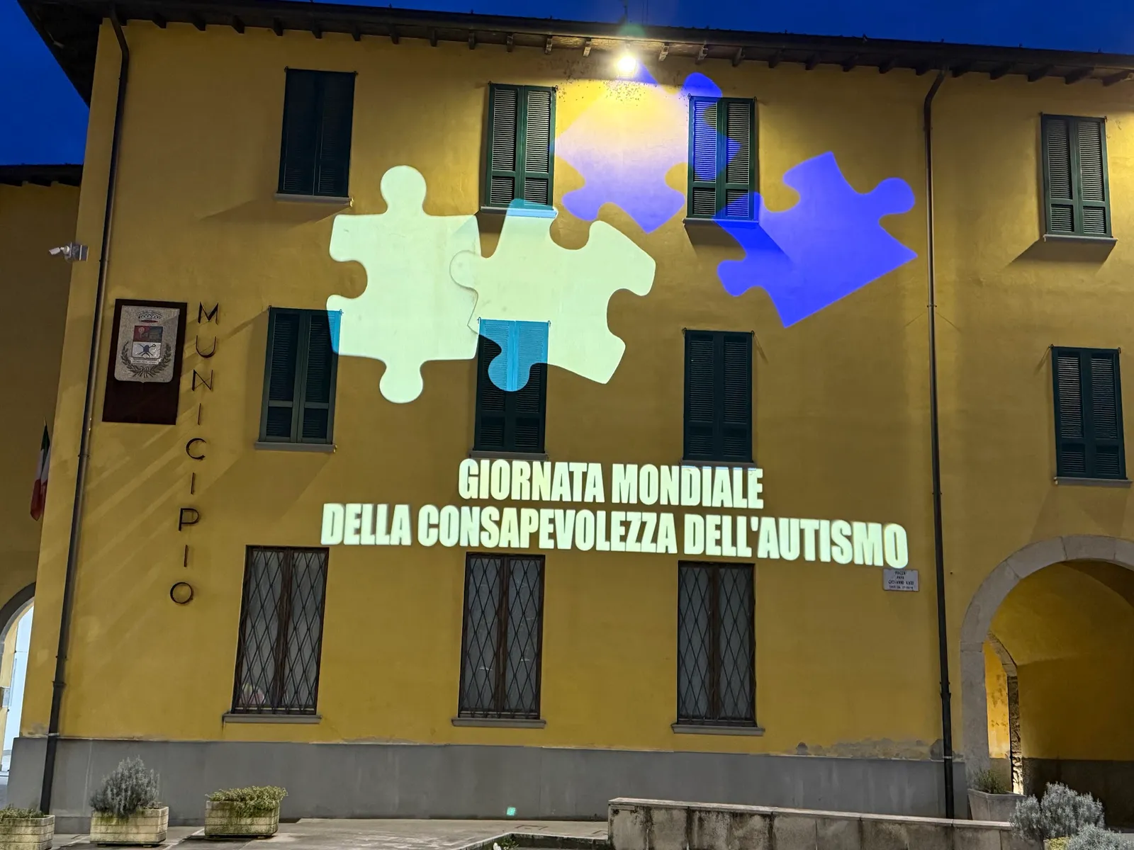 Pezzi di puzzle chiari e blu e la scritta Giornata mondiale della consapevolezza dell'autismo proiettati sulla facciata del municipio di Ghisalba, 1 aprile 2025